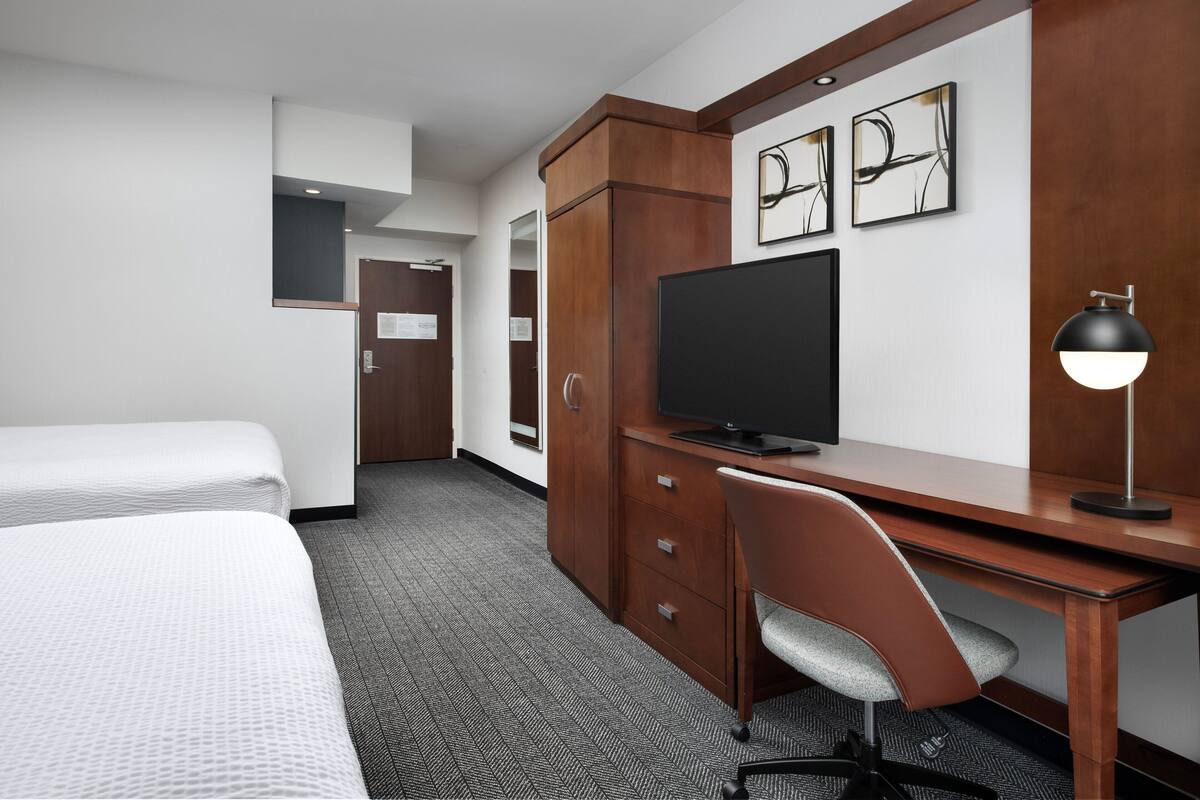 Ein Hotelzimmer mit einem Bett, einem Schreibtisch mit Fernseher, einem Sessel und einem Kleiderschrank.