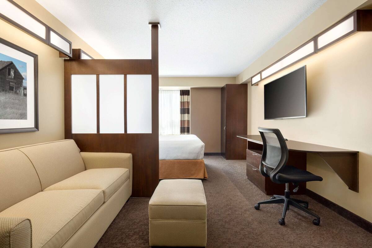 A hotel room with a bed, a desk with a chair, a sofa, and a television.