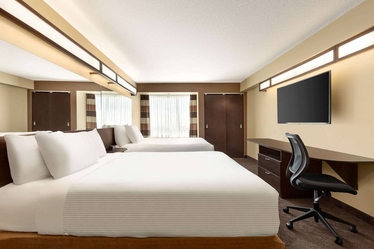 A hotel room with two beds, a desk, a chair, and a flat-screen TV.
