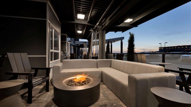 Un espacio moderno para sentarse al aire libre con un hogar de fuego, asientos acolchados y vistas a la ciudad.