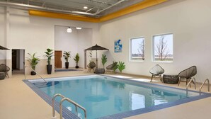 Una piscina interior con agua cristalina y azul, rodeada de plantas en macetas y sillas de mimbre.