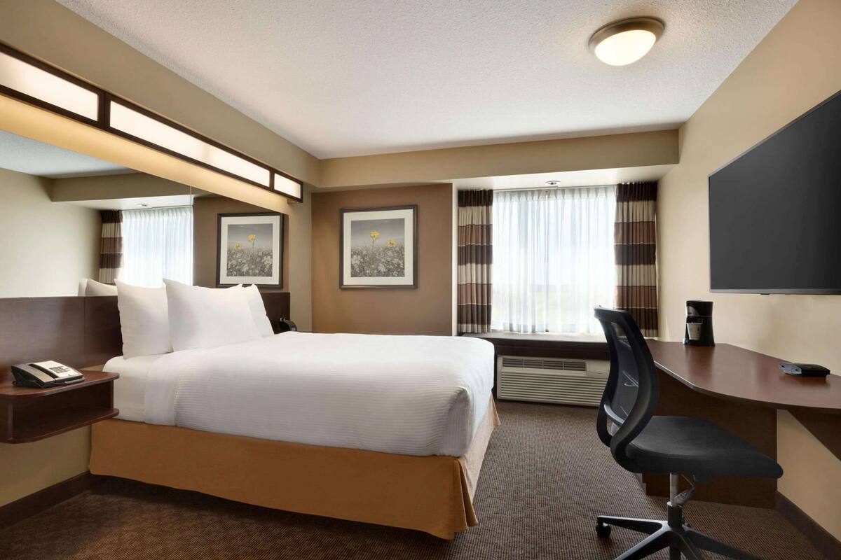 A hotel room with a bed, a desk, a chair, a large mirror, and two framed pictures on the wall.
