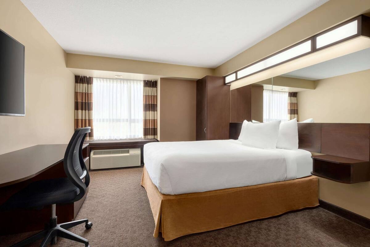 A hotel room with a bed, a desk, a chair, a wardrobe, and a large mirror.