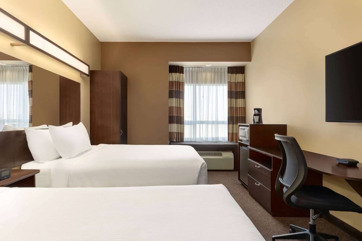 A hotel room with two beds, a desk, a chair, a TV, and a window with curtains.