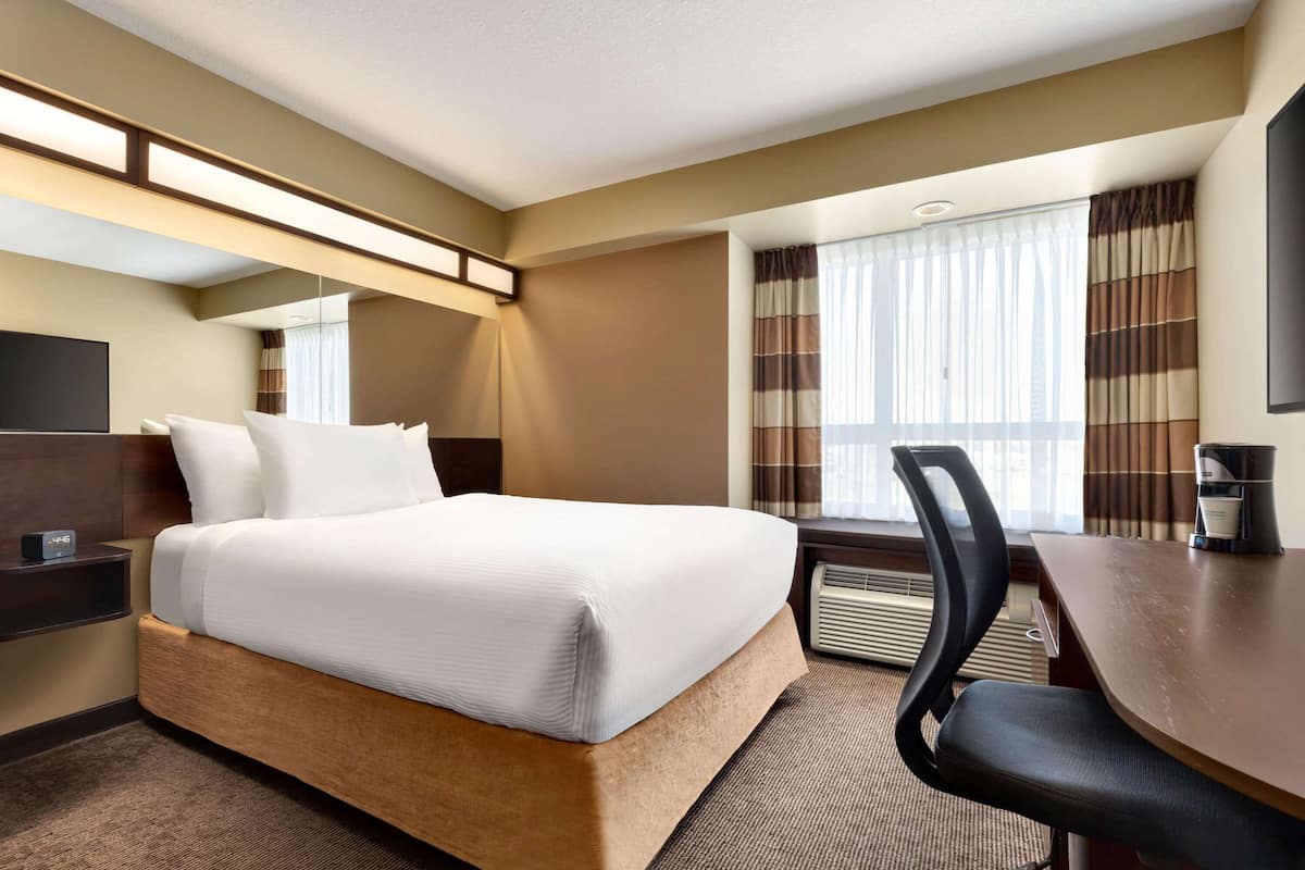 A hotel room with a bed, a desk, a chair, a coffee maker, and a TV.