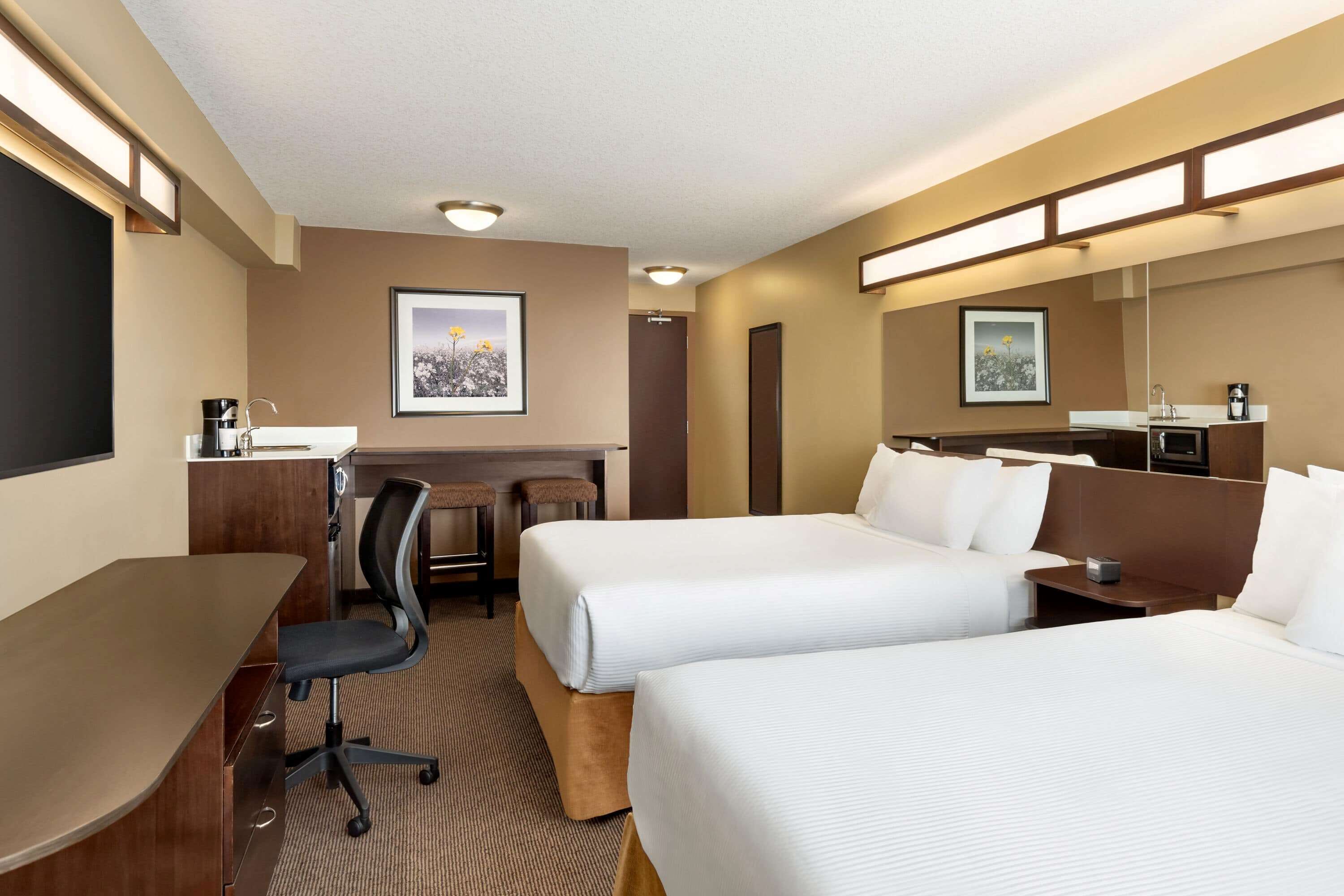 A hotel room with two beds, a desk, a chair, a small table, a mirror, and a picture on the wall.