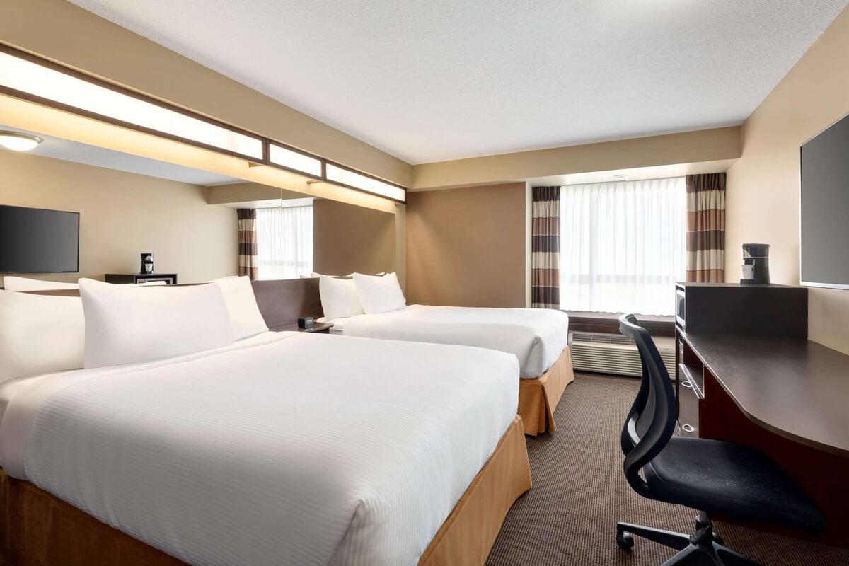 A hotel room with two beds, a desk, a chair, a flat-screen TV, and a coffee maker.