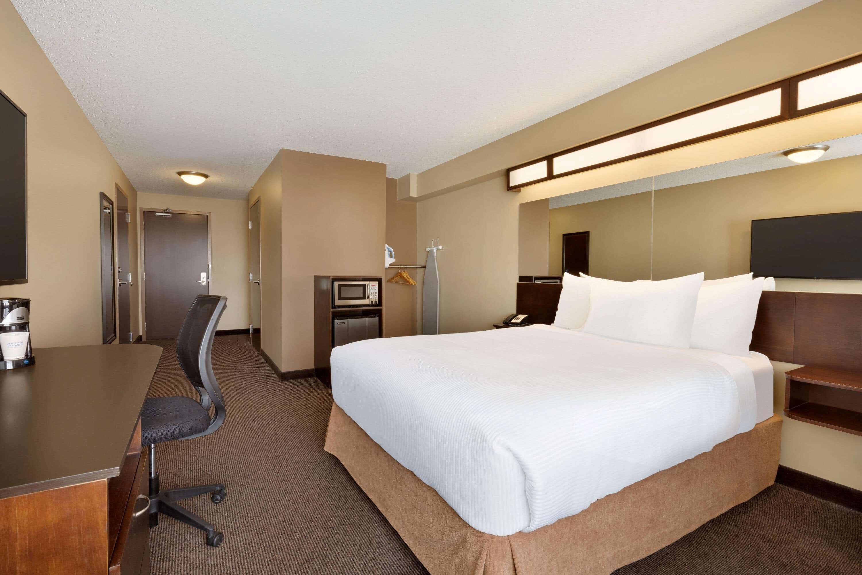 Una habitación de hotel con una cama grande, un escritorio con silla, un televisor y un espejo.
