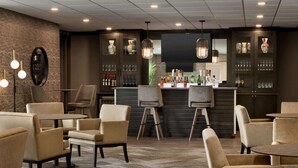 Zona de bar con asientos, barra y estanterías llenas de botellas y vasos.