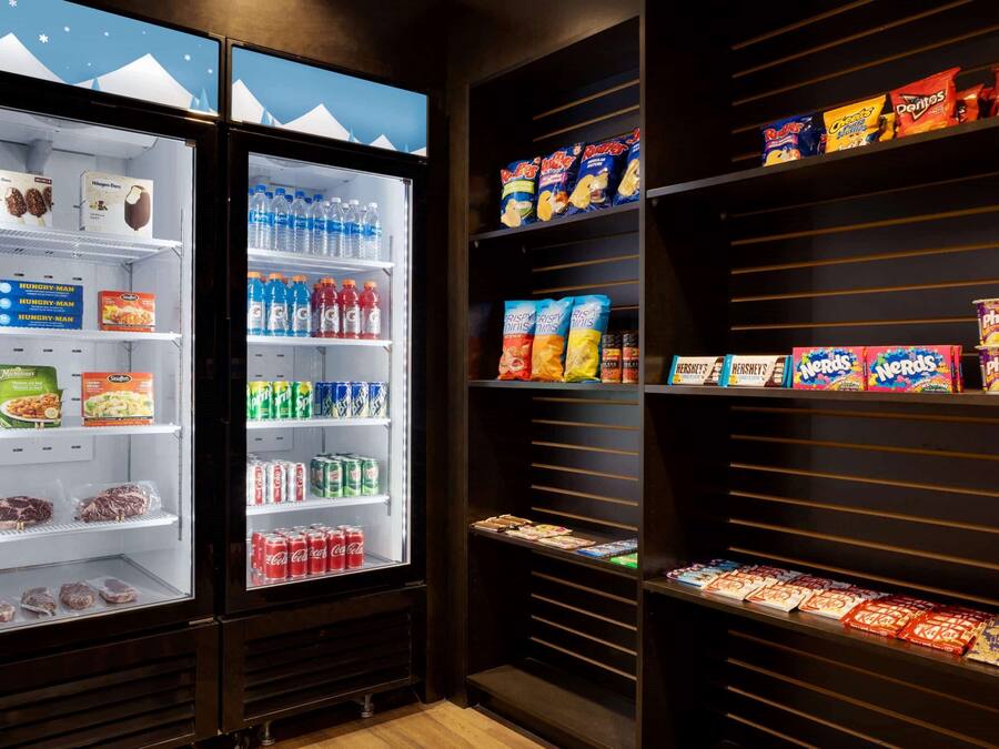Un présentoir réfrigéré contenant divers en-cas et boissons, notamment des chips Doritos, des sodas et du chocolat Hershey's.