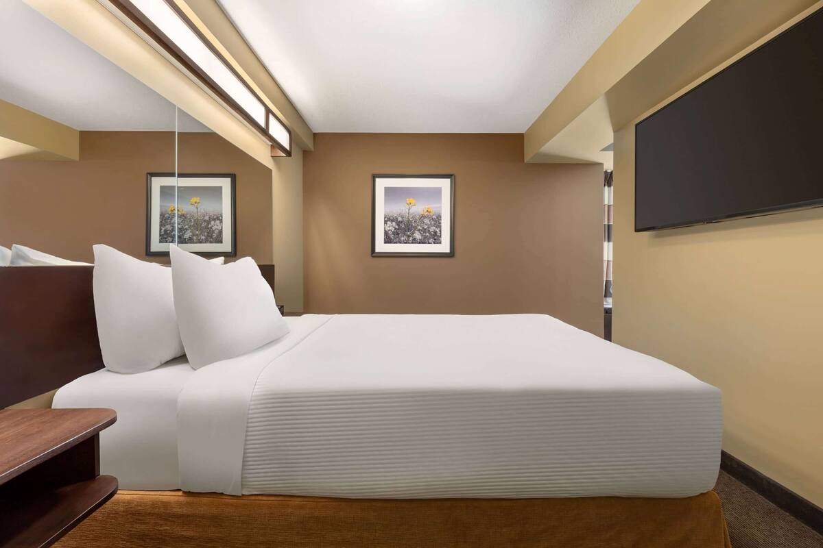 A hotel room with a large bed, a flat-screen TV, and two framed pictures on the wall.