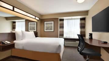 Habitación de hotel con cama, mesita de noche, silla, escritorio y un televisor de pantalla plana grande.