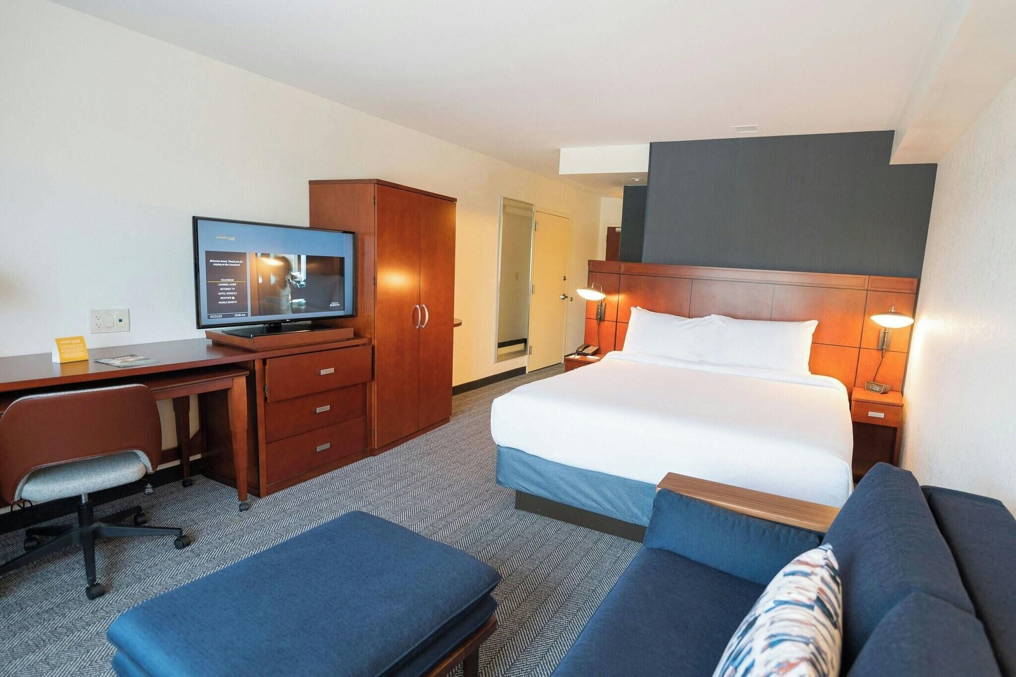 A hotel room with a bed, a desk, a television, a sofa, and a cabinet.