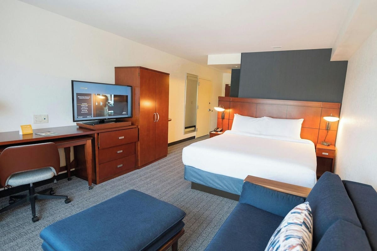 A hotel room with a bed, a desk, a television, a sofa, and a cabinet.