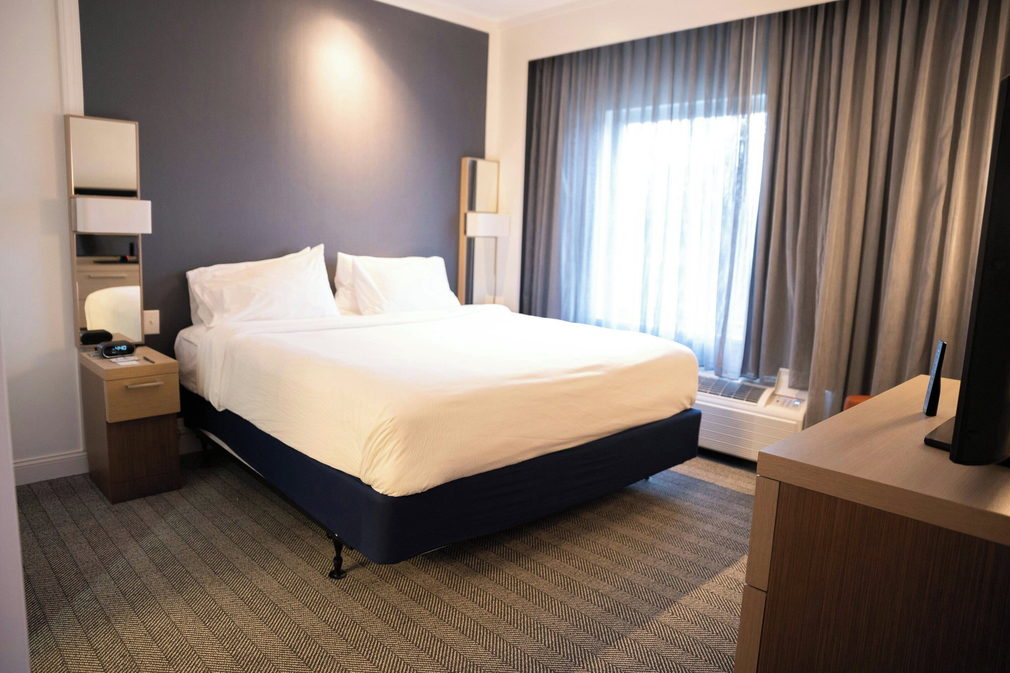Habitación de hotel con una cama grande, mesitas de noche, un escritorio, una lámpara y un ventanal con cortinas.