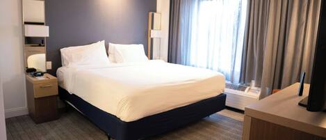 Habitación de hotel con una cama grande, mesitas de noche, un escritorio, una lámpara y un ventanal con cortinas.