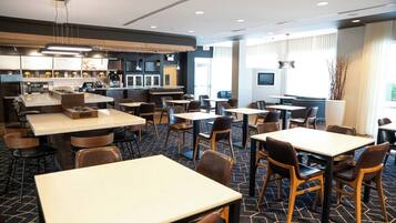 Een moderne hotellobby met meerdere zithoeken, een bar en een zichtbare keuken.
