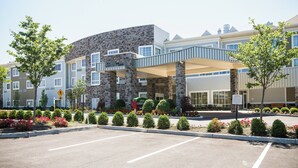 A modern hotel with a stone facade, covered walkway, and landscaped entrance.