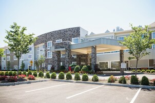 Un hotel moderno con fachada de piedra, pasarela cubierta y entrada ajardinada.