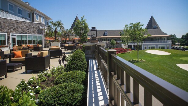 A hotel with outdoor seating, a golf course, and a stone building with a tower.
