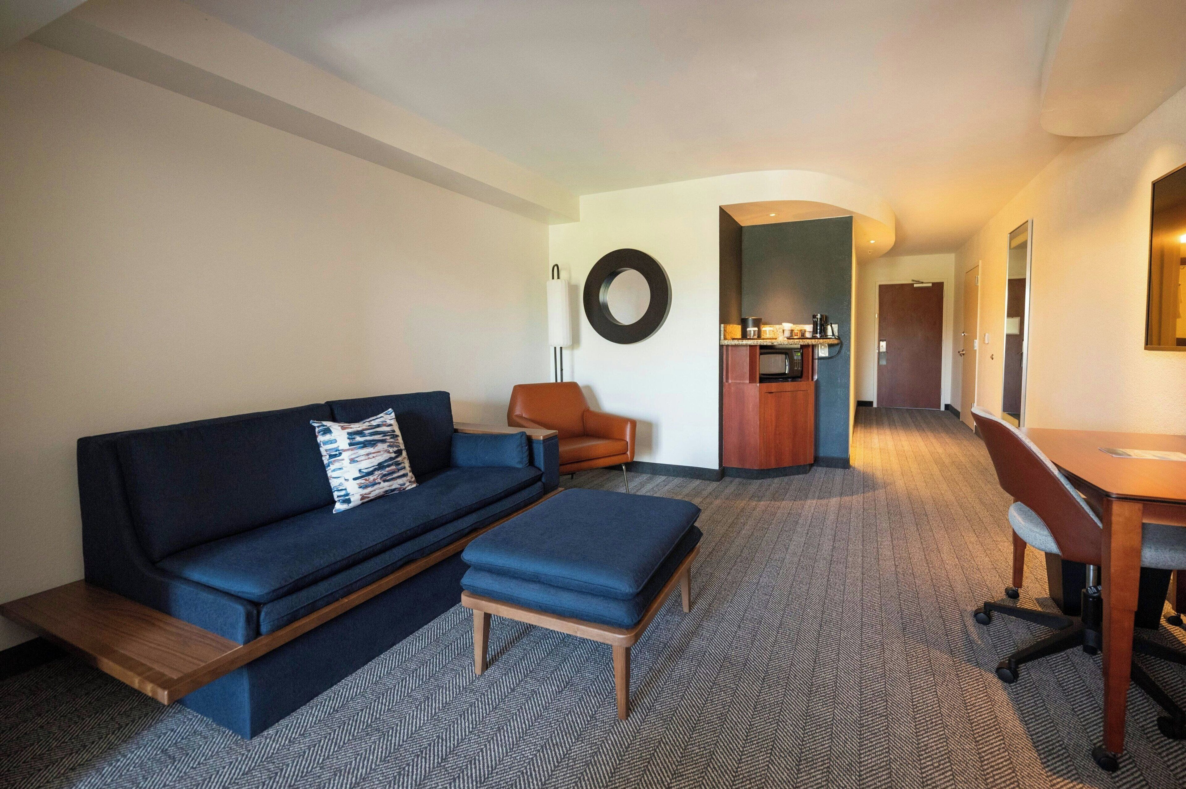 Quarto de hotel moderno com sofá, banquinho e escrivaninha com cadeira.