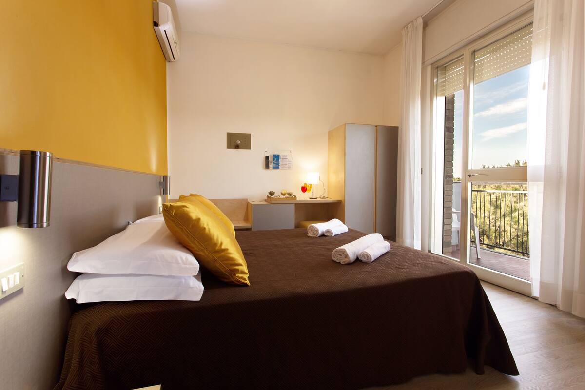 A hotel room with a bed, a desk, a chair, a window with a view, and a balcony.