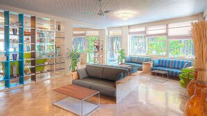 A spacious living area with a large sofa, a coffee table, and a bookshelf filled with books and decorative items. - Hotel Antares (Cervia)