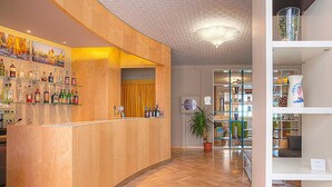 A hotel lobby with a wooden reception desk, a potted plant, and shelves with various items. - Hotel Antares (Cervia)