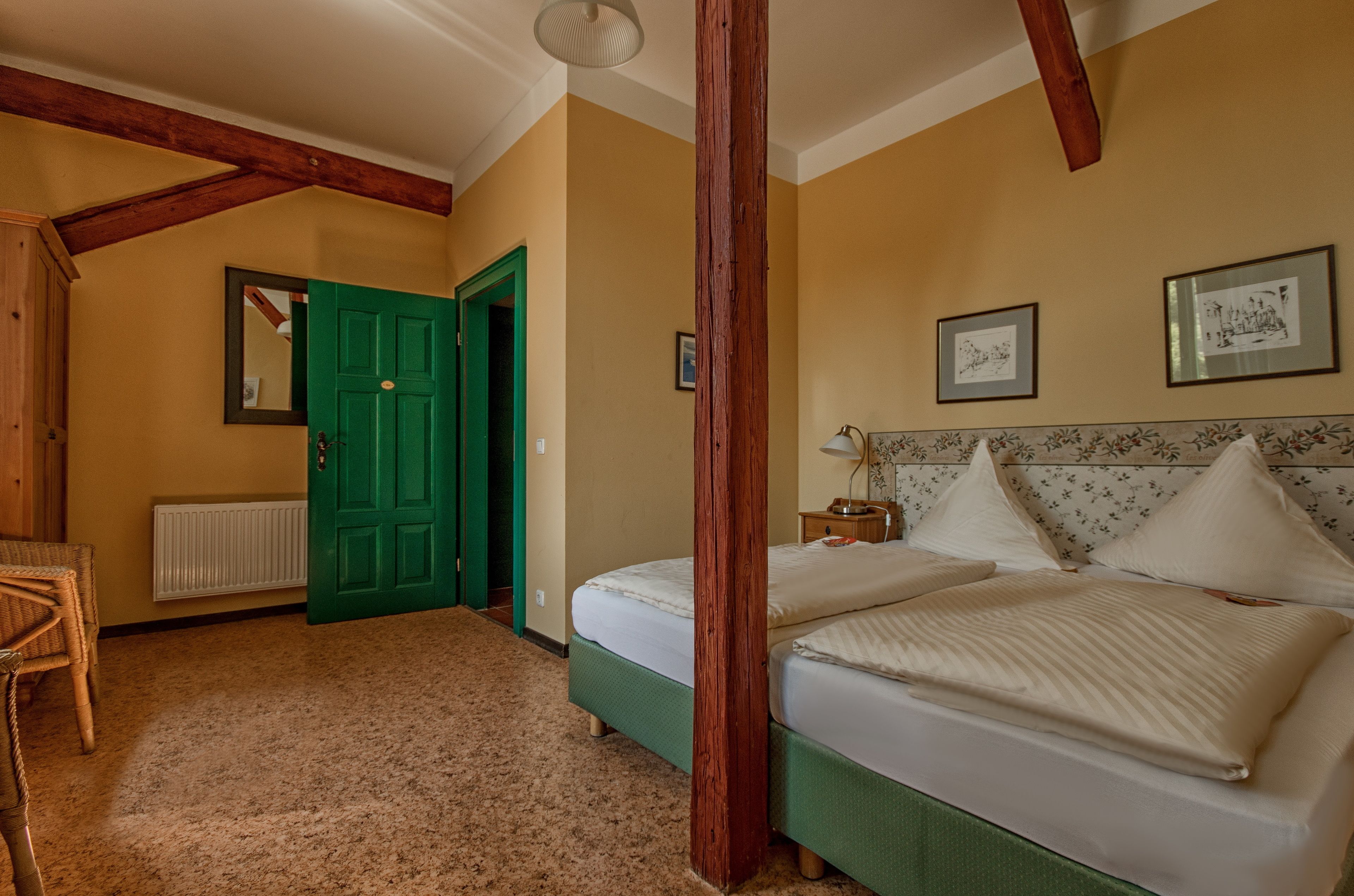 A room with a bed, a green door, a radiator, and framed pictures on the wall.