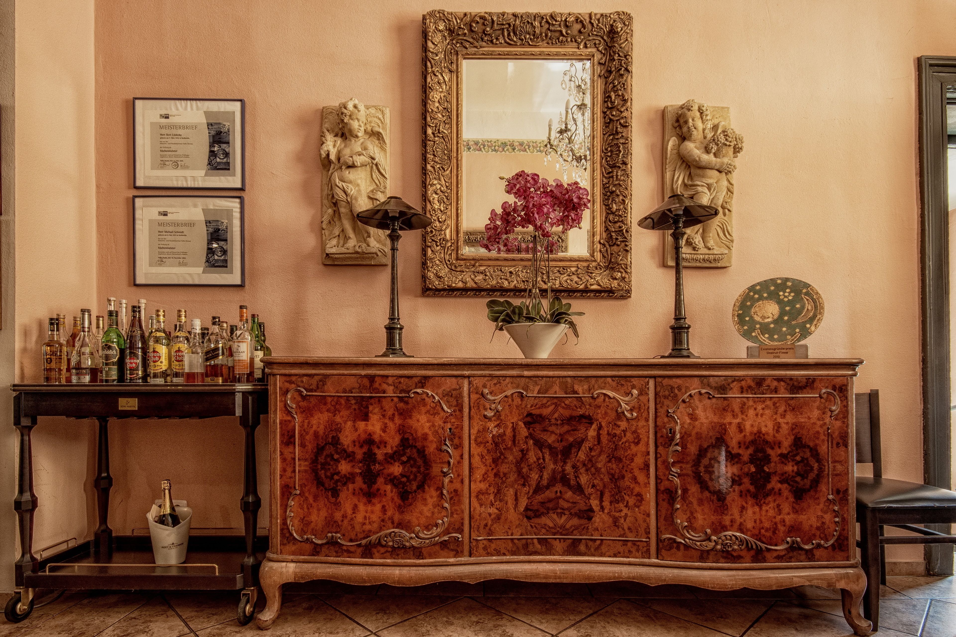 A vintage-style reception desk with a mirror, framed certificates, and decorative statues.