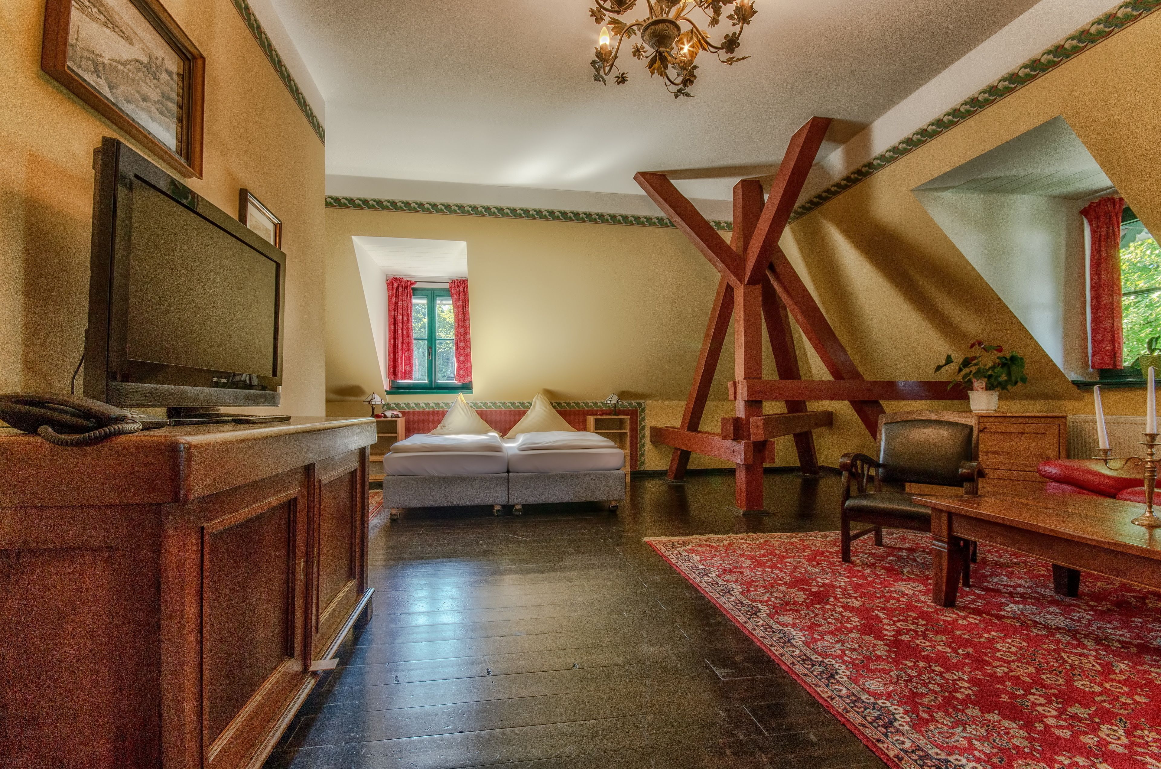 A spacious room with a large bed, a wooden desk, a television, and a chandelier.