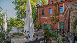 Ein Backsteinhaus mit einer grünen Tür, auf der „SPIEGELSAAL“ steht, und Außenplätzen mit Sonnenschirmen.