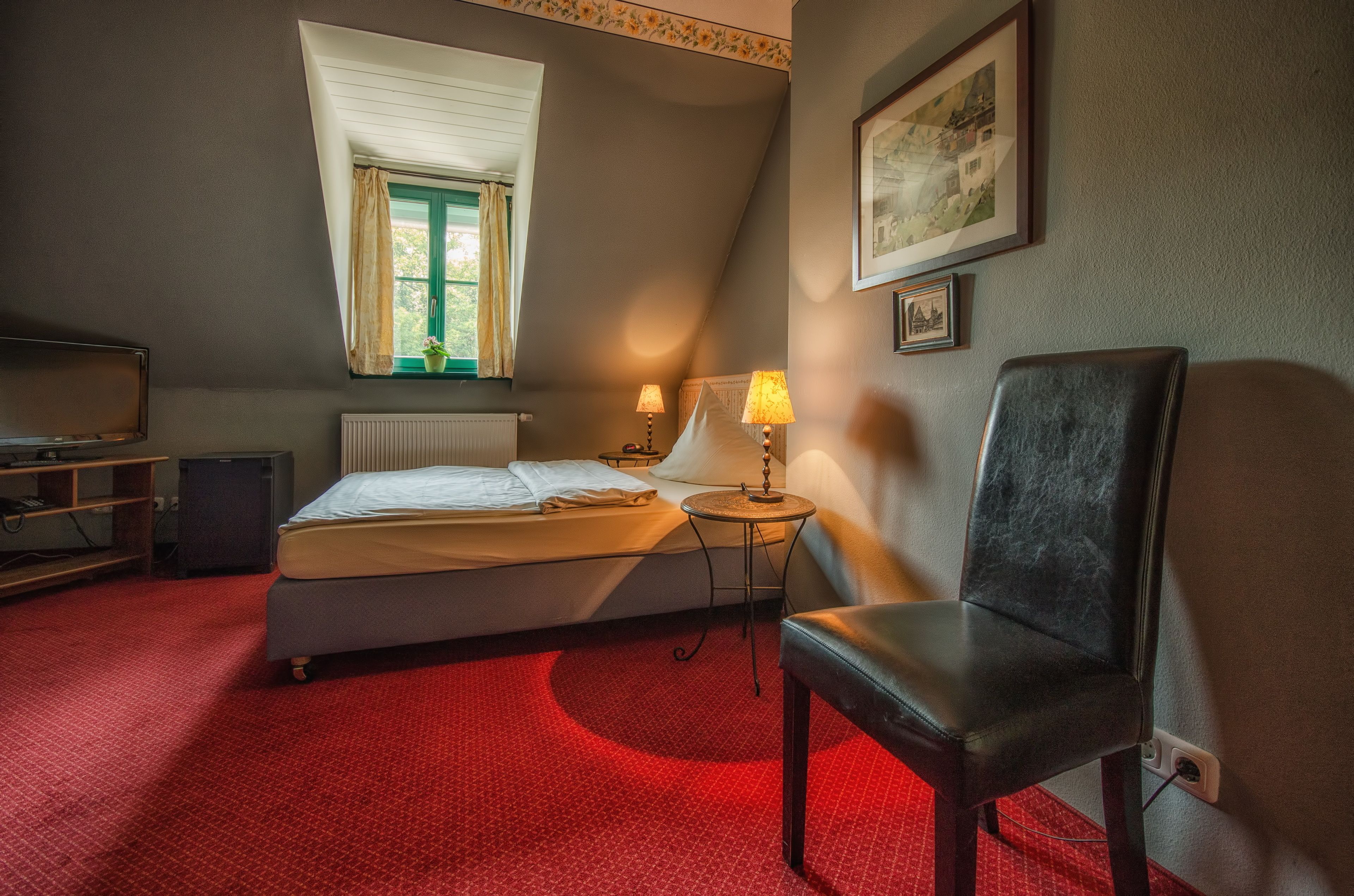 Une chambre à coucher comprenant un lit, une chaise, une lampe, un radiateur, une fenêtre avec des rideaux et un tableau encadré accroché au mur.