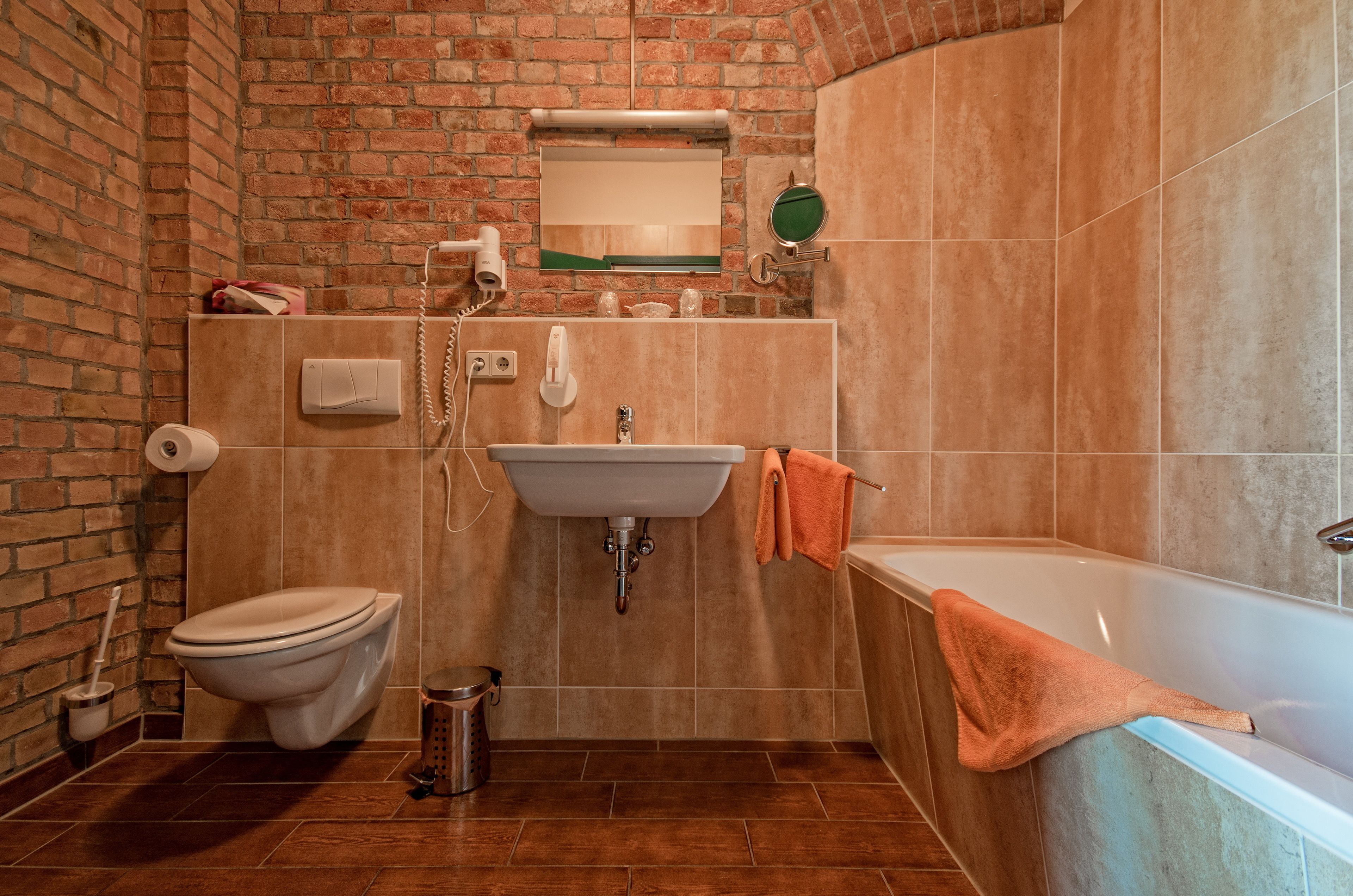 A bathroom with a brick wall, a sink, a toilet, and a bathtub.