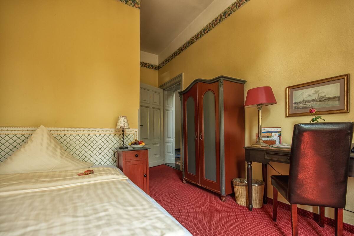 Une chambre d’hôtel comprenant un lit, un bureau avec une lampe, une armoire et une chaise.