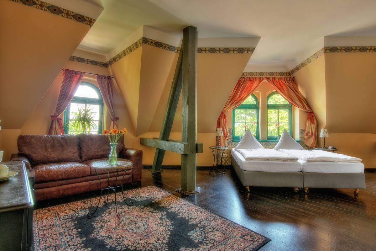 Une pièce avec un canapé en cuir marron, un lit blanc, une grande poutre en bois et un tapis à motifs.