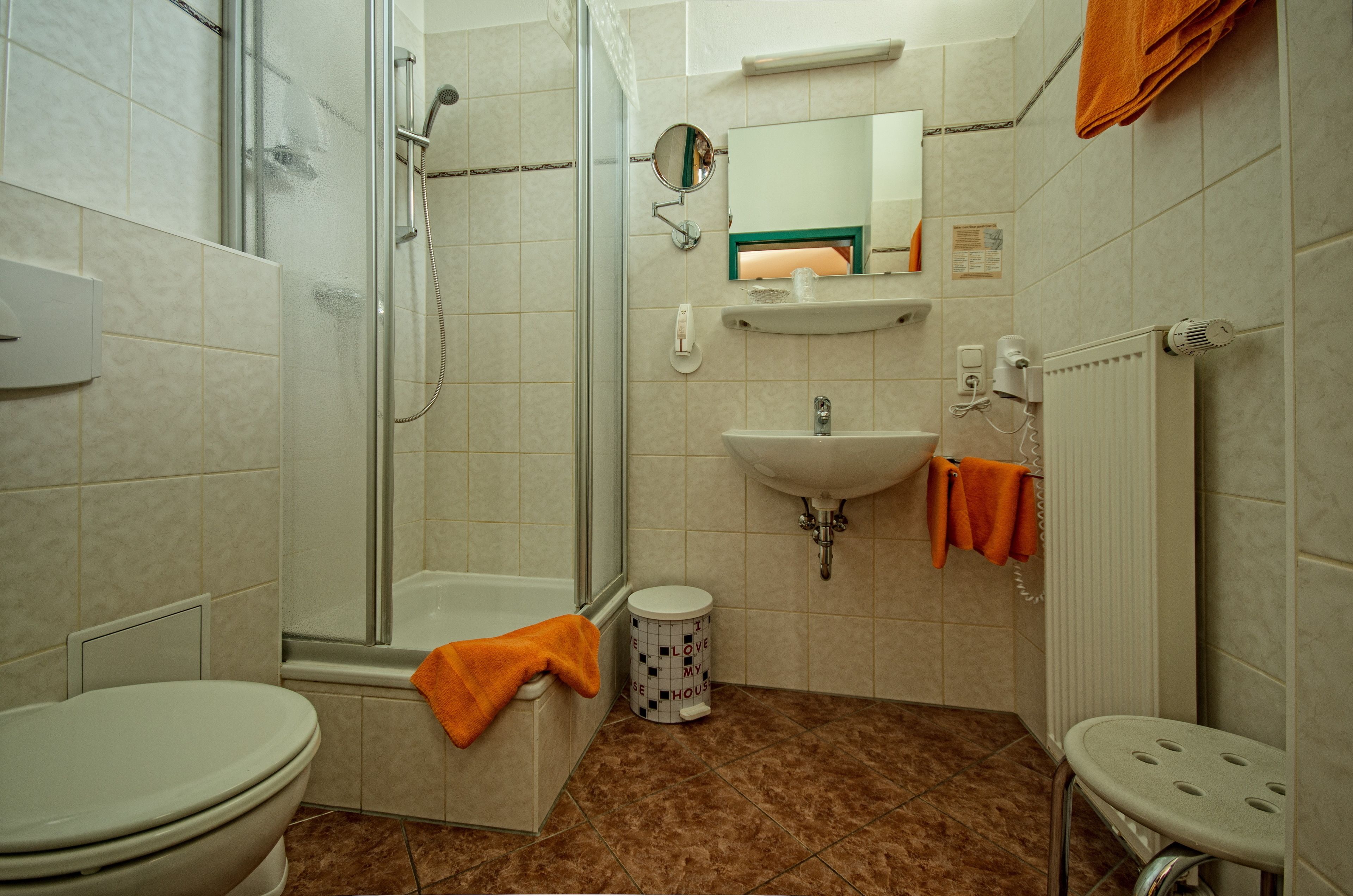 Un baño con inodoro, ducha, lavabo y un taburete pequeño.