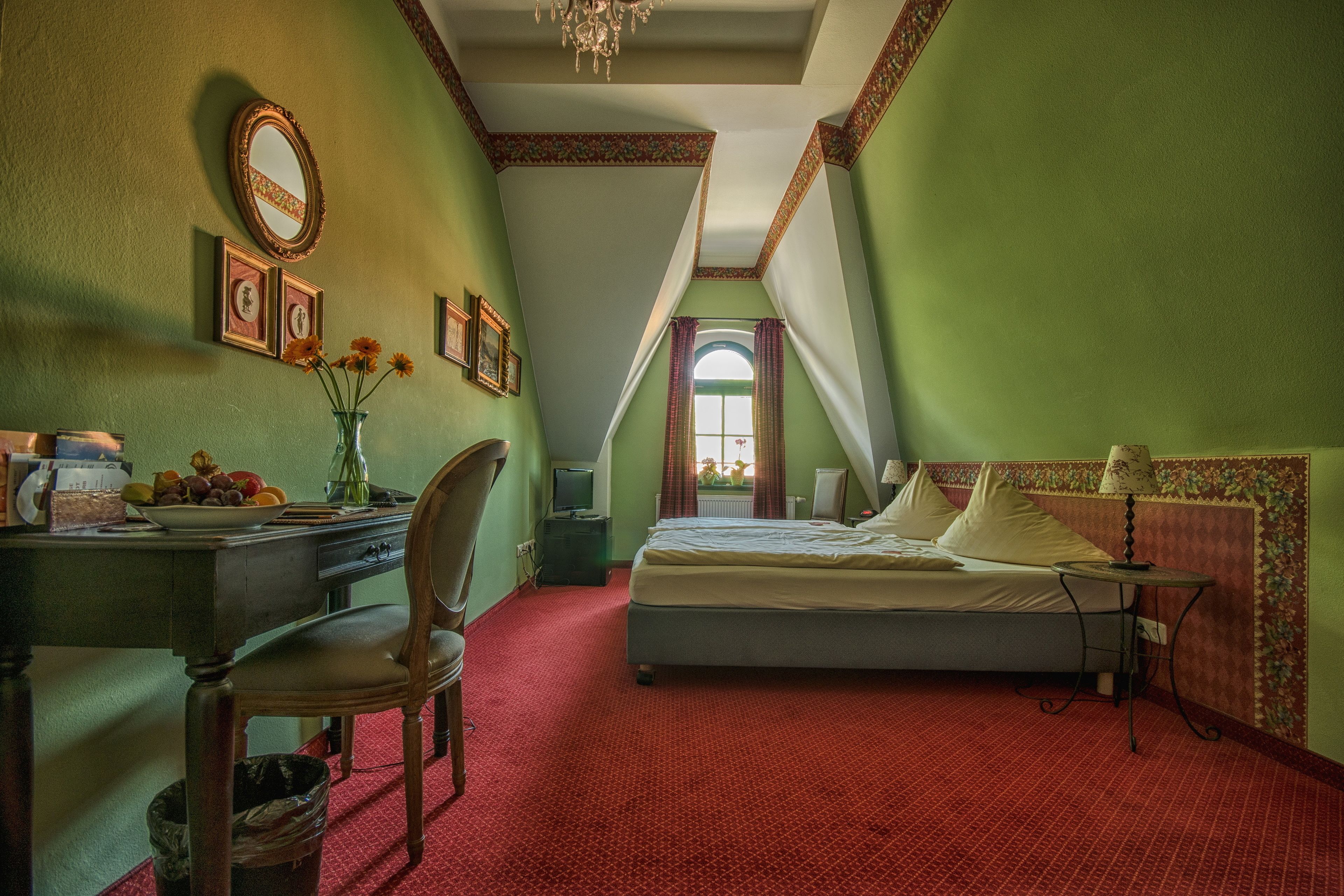 Una habitación con cama, escritorio, silla, mesita y ventana con cortinas.