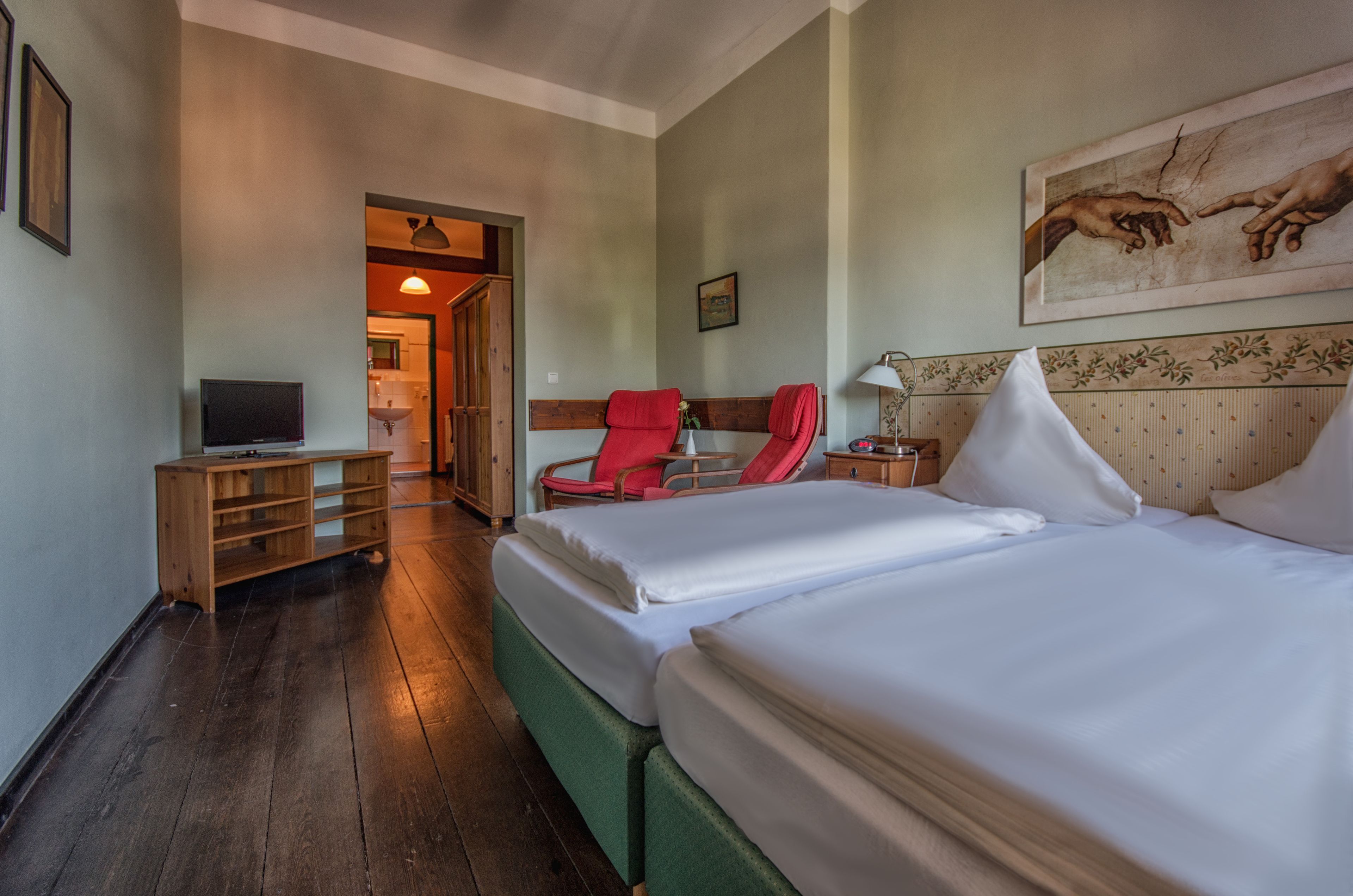 Ein Hotelzimmer mit zwei Betten, einem Fernseher, einem Schreibtisch, einem Stuhl und einem Bild an der Wand.
