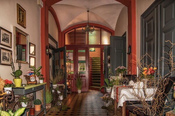 A hallway with a checkered floor, wooden doors, and various potted plants.