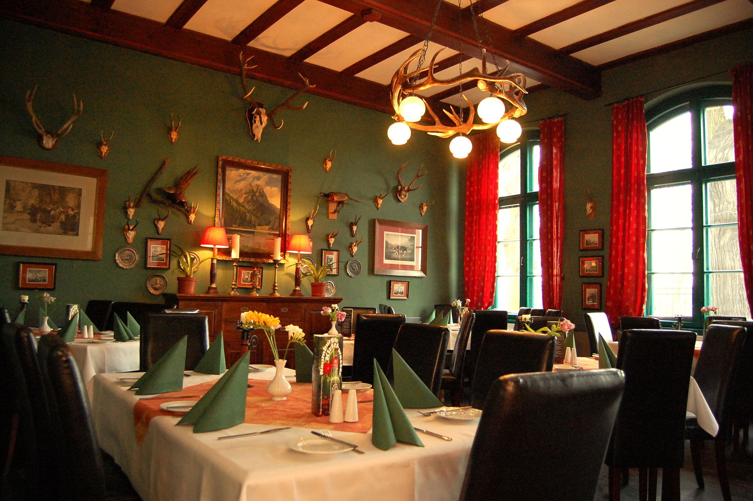 A dining room with tables set for service, a chandelier, and wall-mounted animal skulls.