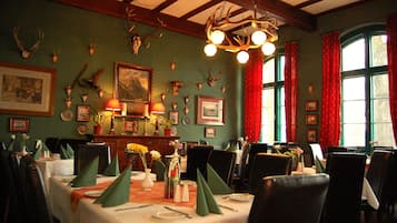 A dining room with tables set for service, a chandelier, and wall-mounted animal skulls.