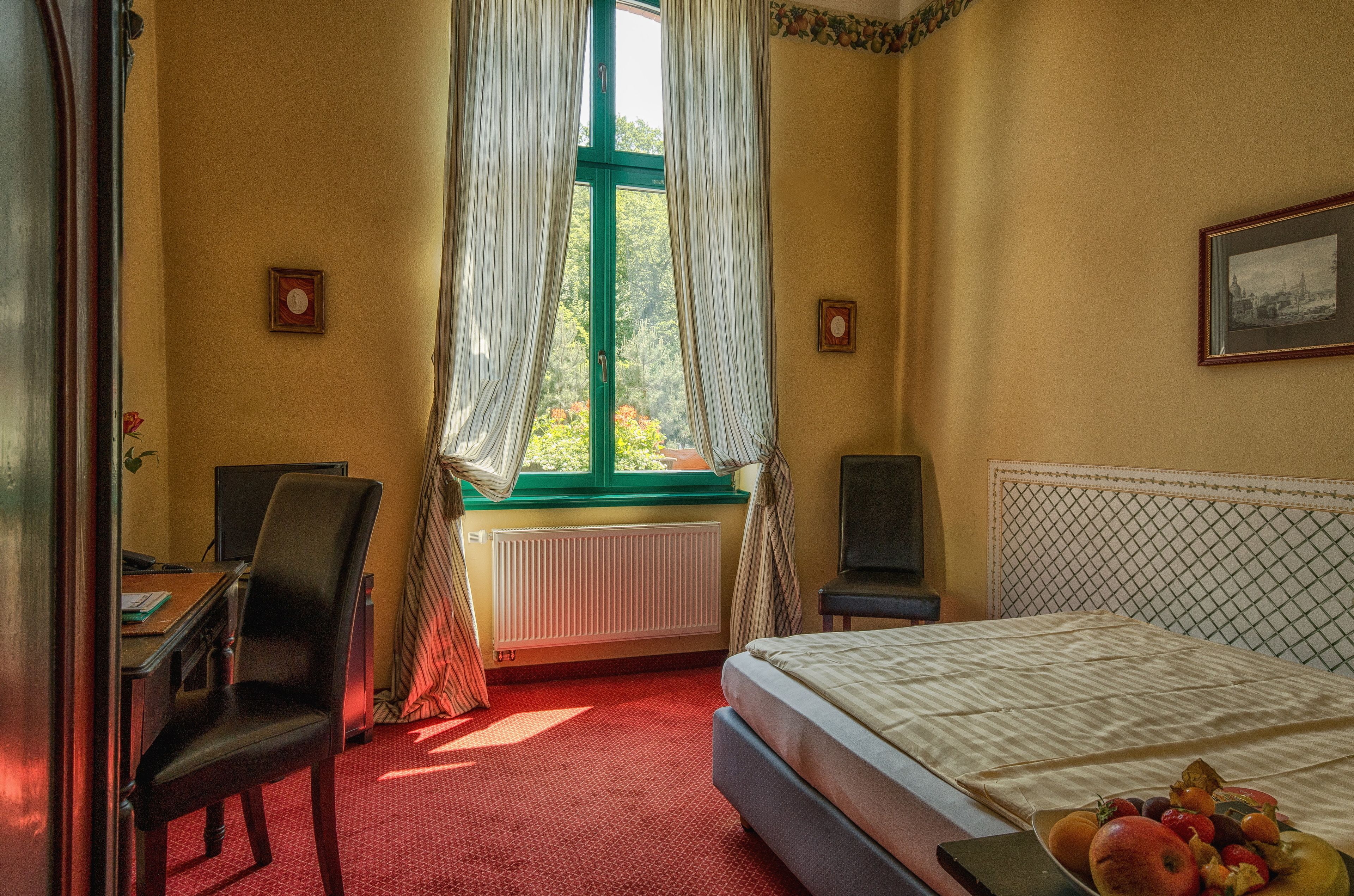 Une chambre d’hôtel avec un lit, un bureau, une chaise, un radiateur et une fenêtre avec des rideaux.