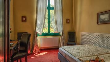 Une chambre d’hôtel avec un lit, un bureau, une chaise, un radiateur et une fenêtre avec des rideaux.