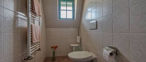A compact bathroom with a toilet, a towel rack, a small window, and a toilet paper holder.