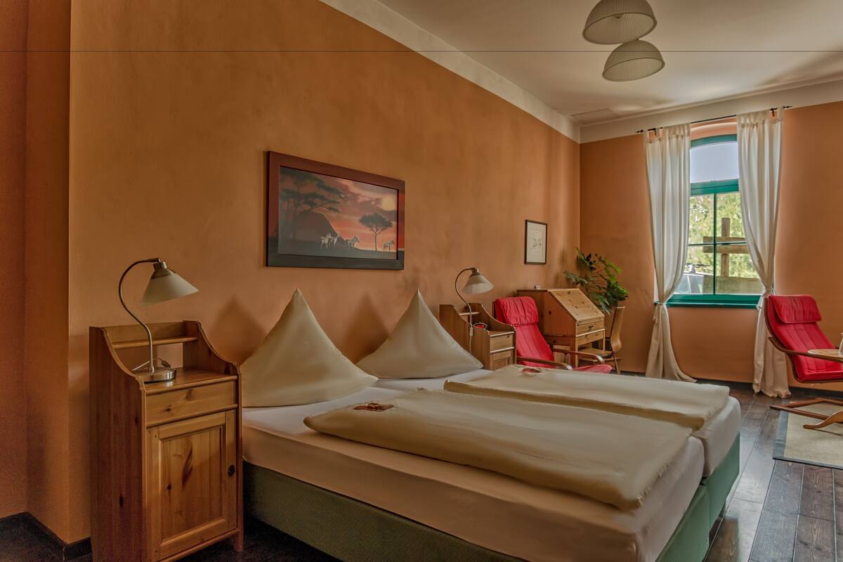 Une chambre d’hôtel avec deux lits, une table de chevet, un bureau, une chaise et une fenêtre avec des rideaux.