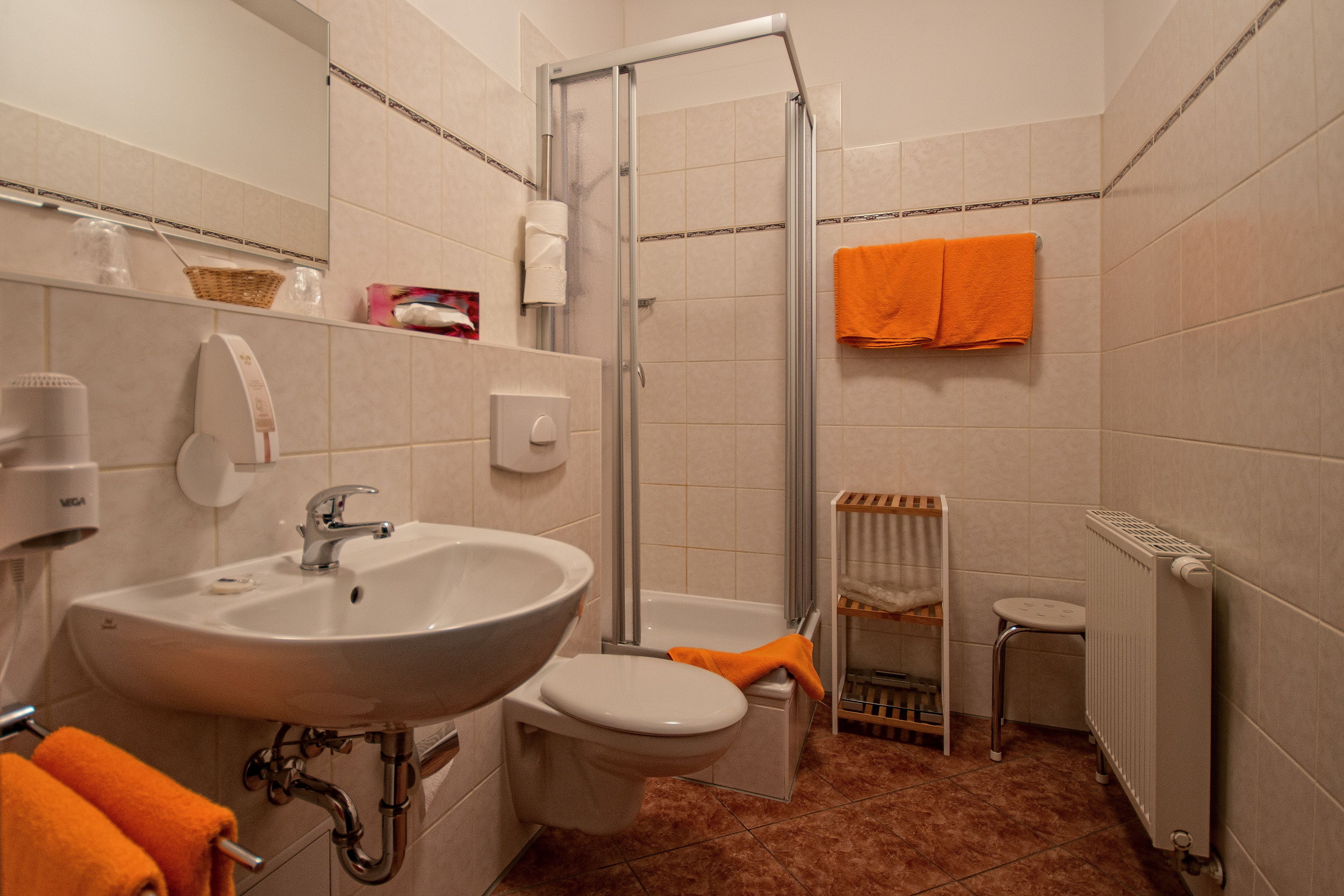 A bathroom with a sink, toilet, and shower. There are towels and a basket on the counter.