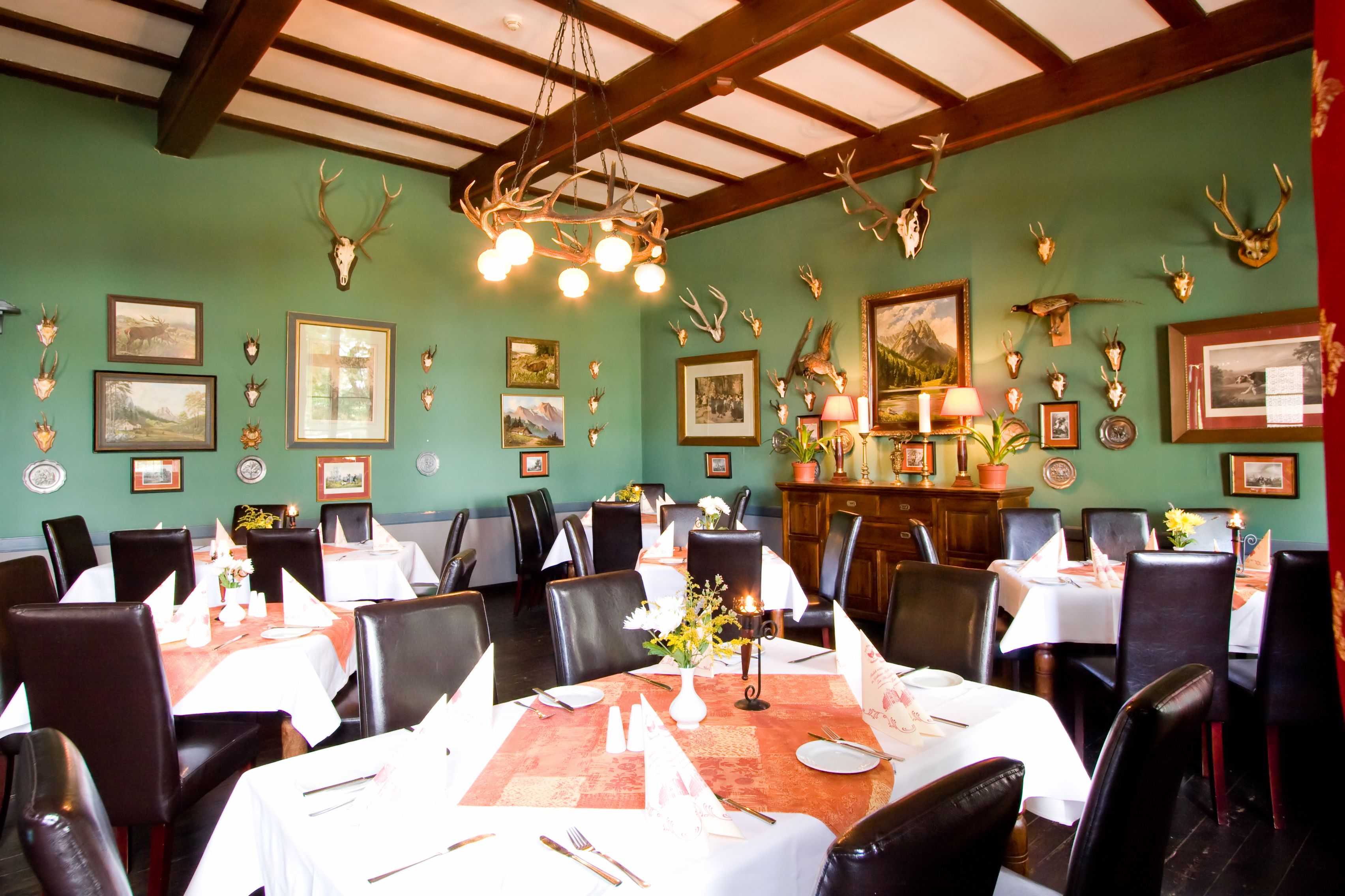 A dining area with tables set for service, surrounded by chairs, and decorated with antler wall art and framed pictures.