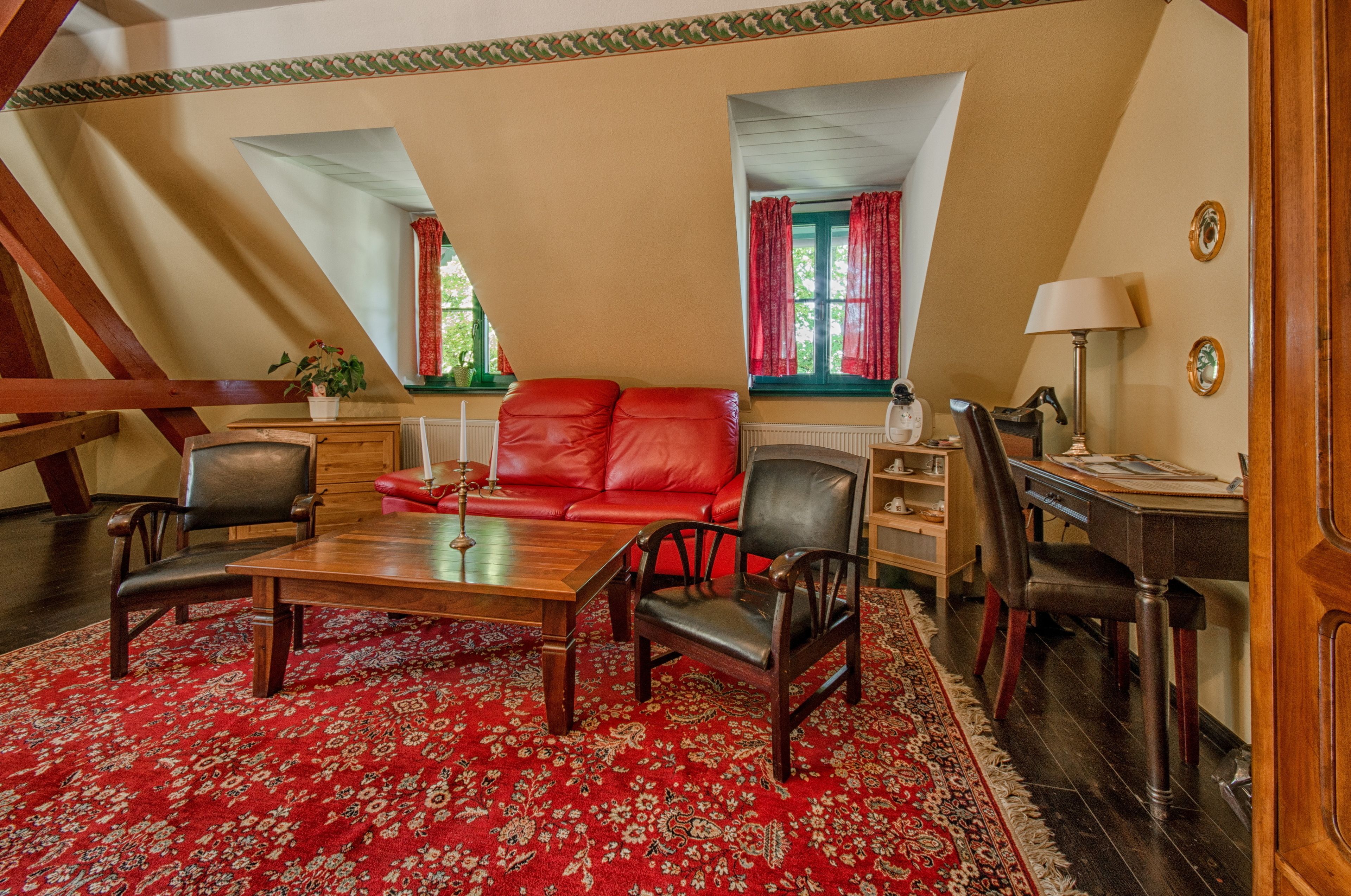 A room with a red sofa, wooden table, and chairs, a radiator, and a desk with a lamp.