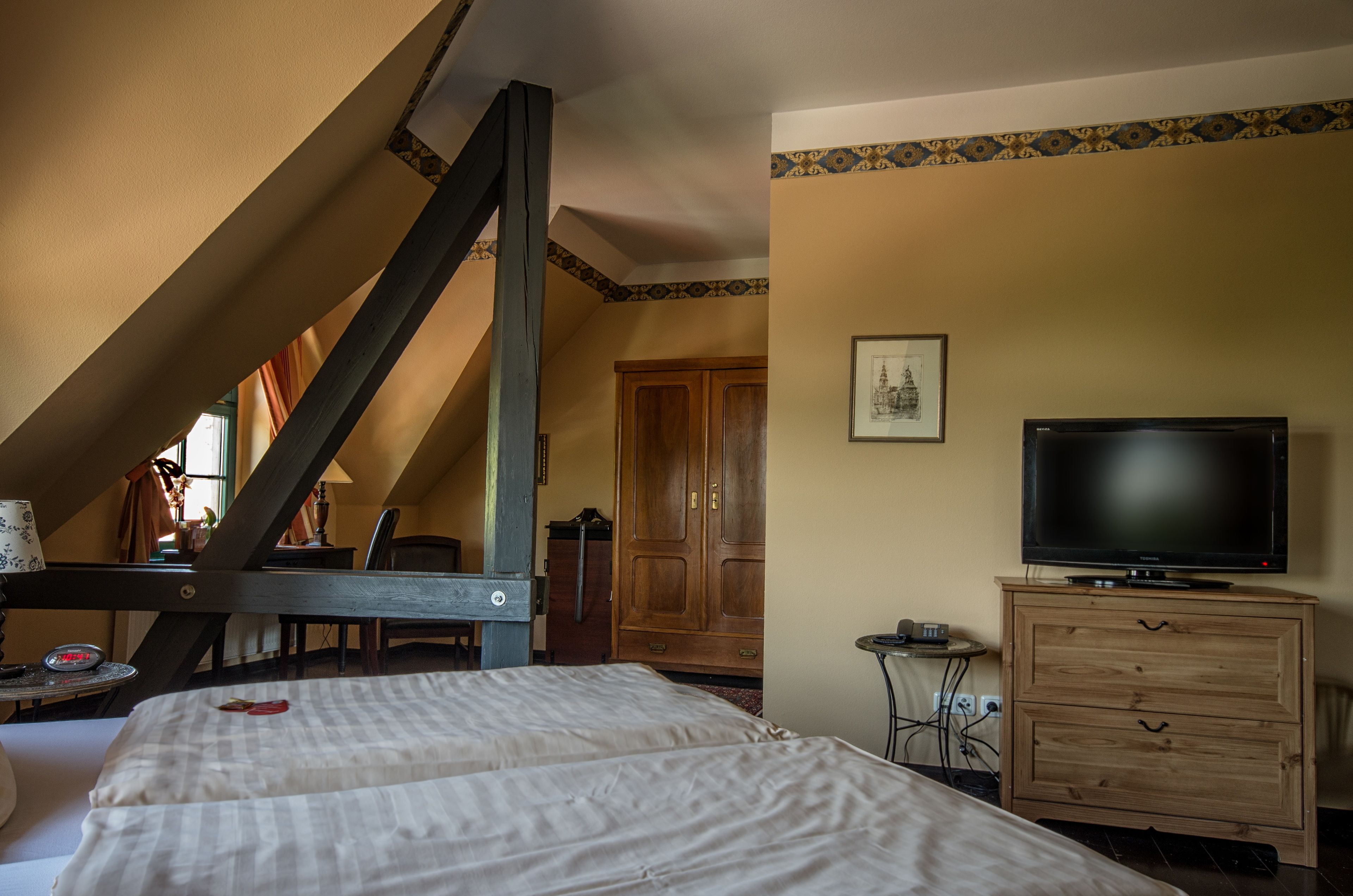 Ein Schlafzimmer mit schrägen Wänden, einem Holzschrank, einem Fernseher und einem Bett mit karierter Bettdecke.